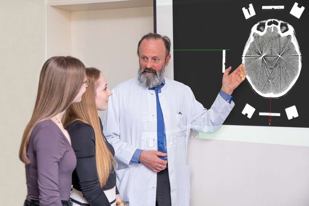 Professor Krauss sieht sich mit Jette (links) und Nele die Aufnahme eines Gehirns an. Die Elektroden des Neurostimulationssystems sind als weiße Punkte erkennbar.